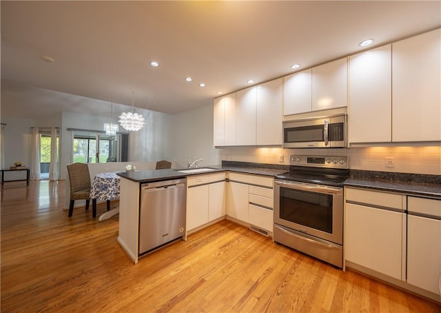 kitchen with stainless steel appliances, dark countertops, light wood-style flooring, and a peninsula