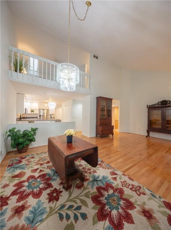 living area with an inviting chandelier, a high ceiling, light wood finished floors, and visible vents
