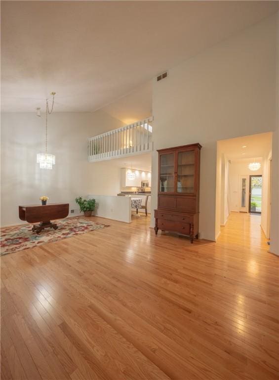 living room with high vaulted ceiling, a notable chandelier, light wood-type flooring, and visible vents