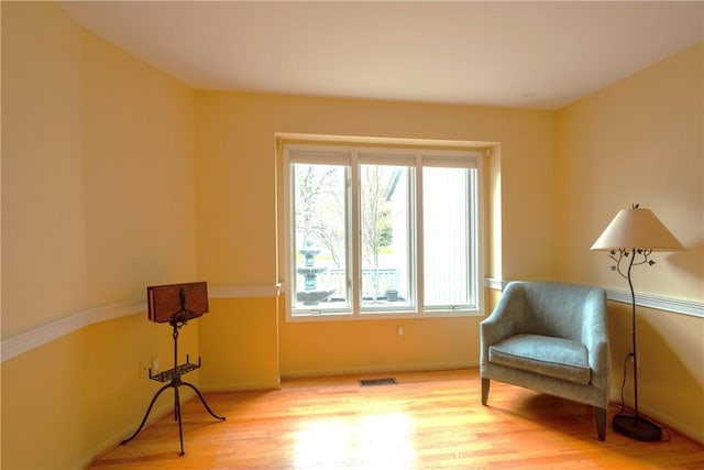 living area with a healthy amount of sunlight, baseboards, wood finished floors, and visible vents