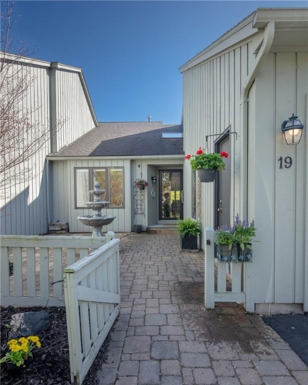 doorway to property with roof with shingles, board and batten siding, and a patio area