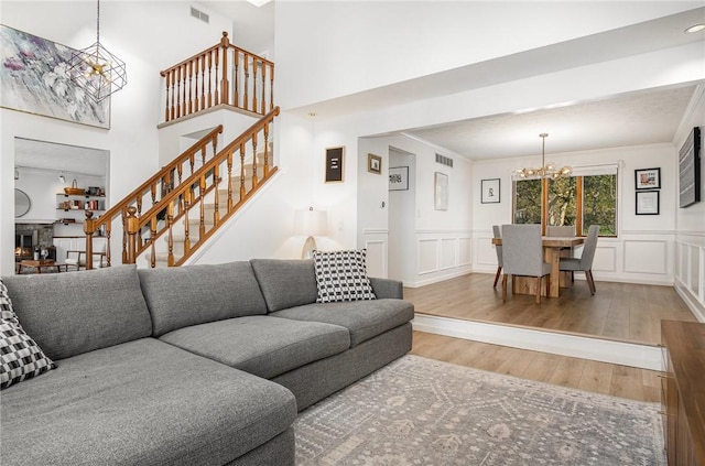 living area featuring visible vents, stairs, a decorative wall, wood finished floors, and a notable chandelier