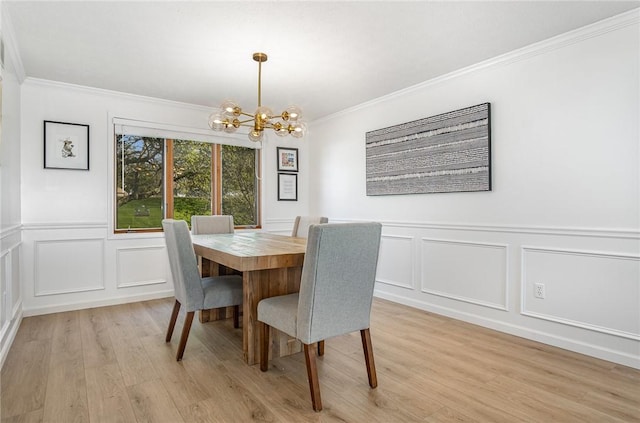dining space featuring light wood-style floors, ornamental molding, a decorative wall, and a chandelier