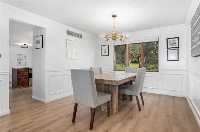 dining space with crown molding, an inviting chandelier, a decorative wall, light wood-type flooring, and visible vents
