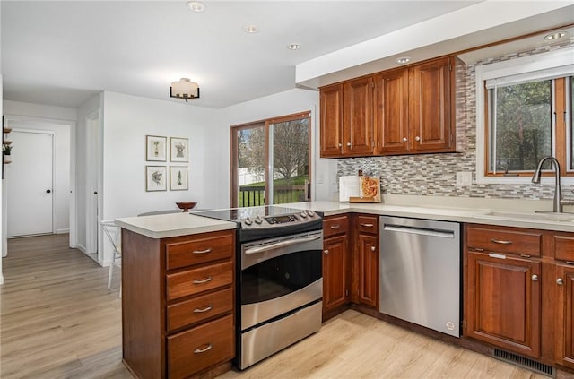 kitchen with light wood-style floors, a sink, appliances with stainless steel finishes, and a peninsula