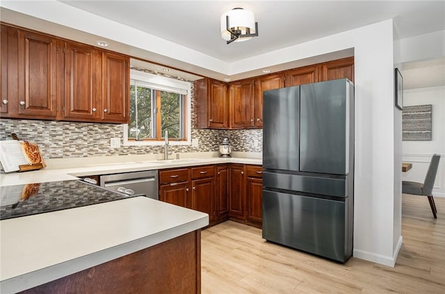 kitchen with backsplash, stainless steel appliances, a sink, and light wood finished floors