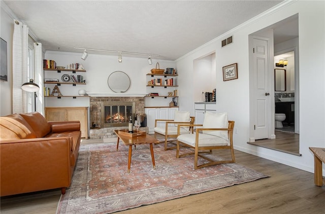 living area with a fireplace, rail lighting, wood finished floors, visible vents, and ornamental molding