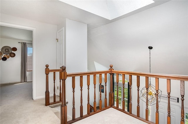 hallway featuring a skylight, carpet floors, baseboards, and an upstairs landing