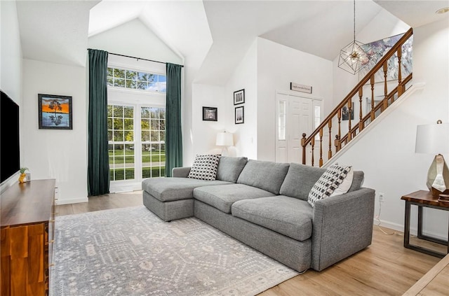 living room featuring an inviting chandelier, wood finished floors, baseboards, high vaulted ceiling, and stairway