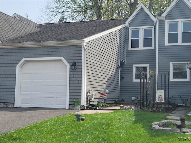 view of side of property featuring a shingled roof, an attached garage, a yard, and driveway