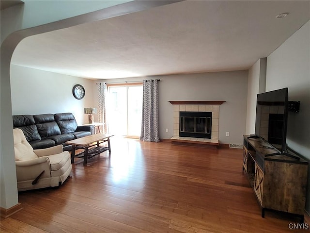 living area with arched walkways, wood finished floors, and a tile fireplace