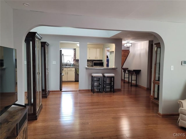 living area with arched walkways, baseboards, and wood finished floors