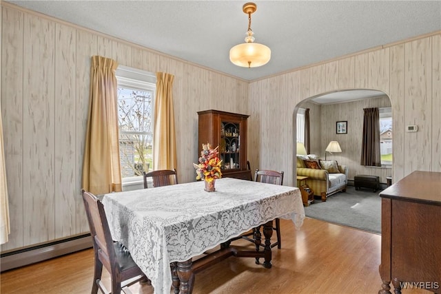 dining area featuring crown molding, arched walkways, a baseboard heating unit, and a wealth of natural light
