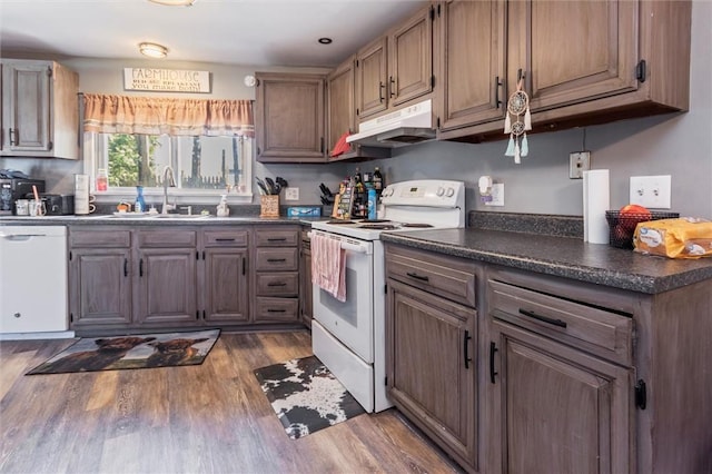 kitchen with dark countertops, wood finished floors, a sink, under cabinet range hood, and white appliances