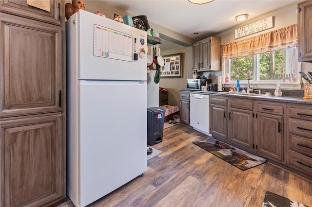kitchen with a sink, dark countertops, wood finished floors, and white appliances