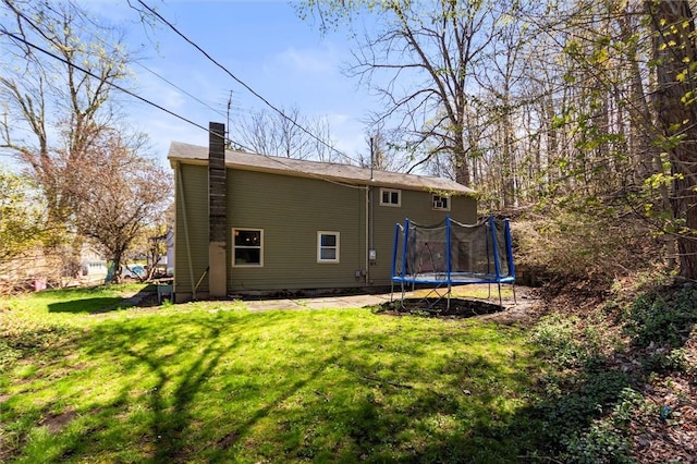 rear view of house featuring a lawn, a chimney, and a trampoline