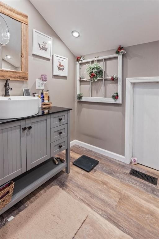 bathroom with vanity, visible vents, lofted ceiling, wood finished floors, and baseboards