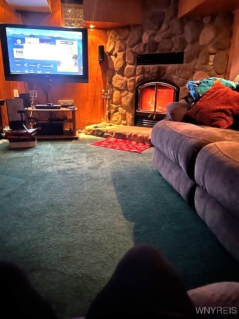 interior space with carpet floors, wooden walls, and a stone fireplace