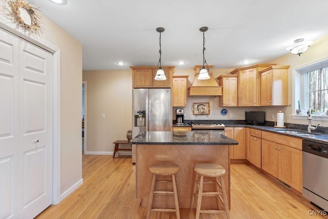 kitchen with a center island, a sink, premium range hood, stainless steel appliances, and light wood-style flooring