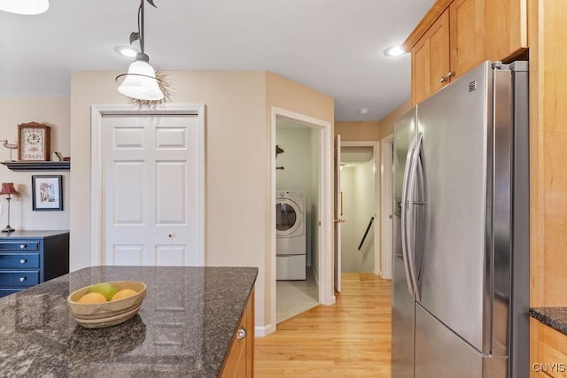 kitchen with washer / dryer, stainless steel fridge with ice dispenser, dark stone countertops, and light wood-style flooring