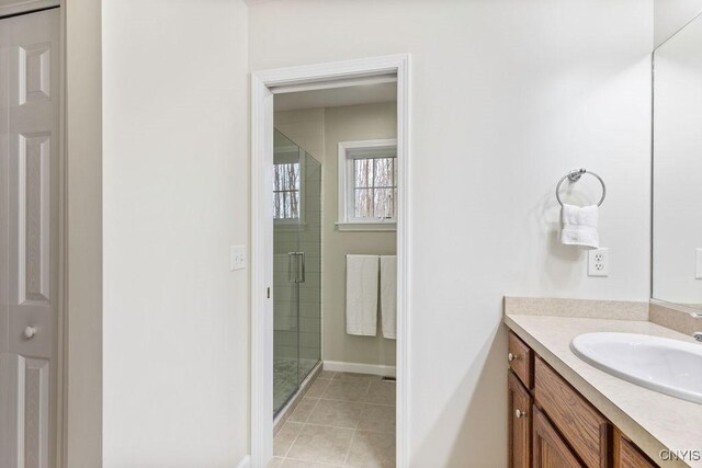 full bath featuring vanity, tile patterned floors, baseboards, and a stall shower
