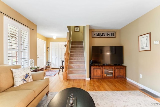 living area featuring baseboards, visible vents, wood finished floors, and stairway