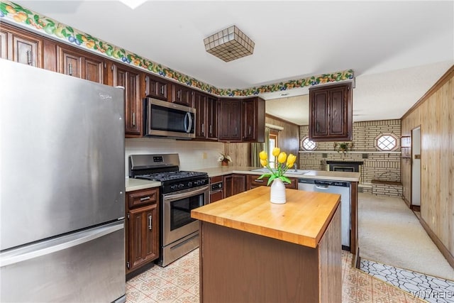 kitchen featuring a brick fireplace, stainless steel appliances, dark brown cabinetry, and wooden counters