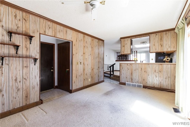 unfurnished living room featuring visible vents, baseboards, wooden walls, a ceiling fan, and carpet