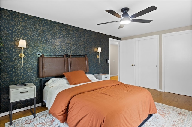 bedroom featuring a ceiling fan, multiple closets, and wood finished floors