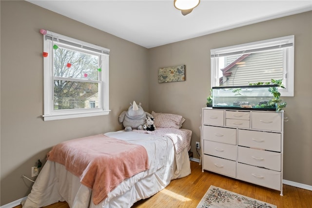 bedroom with baseboards, light wood finished floors, and multiple windows