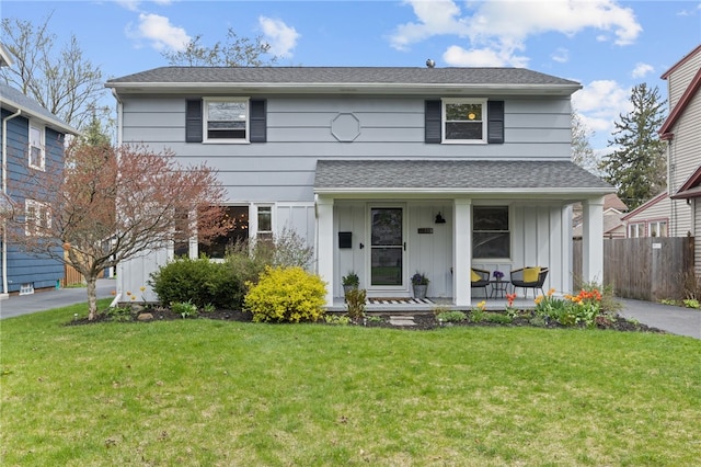 traditional-style home featuring a front lawn, fence, covered porch, a shingled roof, and board and batten siding