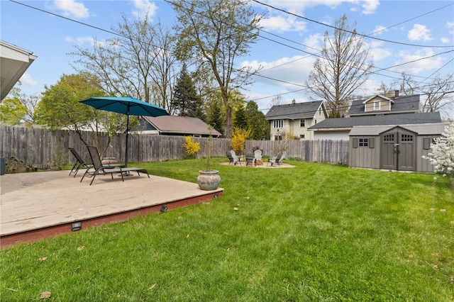 view of yard featuring an outdoor structure, a fire pit, a wooden deck, a fenced backyard, and a storage shed