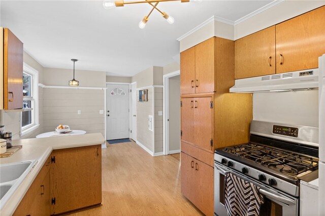 kitchen featuring light wood finished floors, stainless steel gas stove, light countertops, decorative light fixtures, and under cabinet range hood