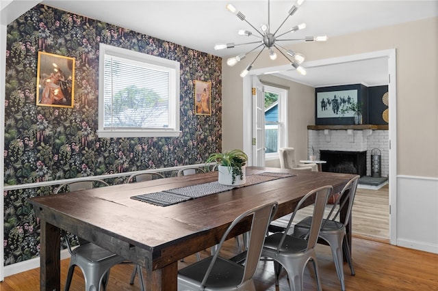 dining area with light wood finished floors, a brick fireplace, a notable chandelier, and wallpapered walls