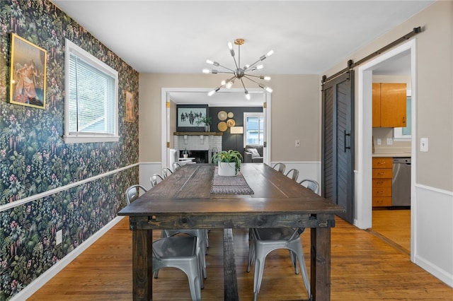 dining area featuring wallpapered walls, a barn door, a wainscoted wall, light wood finished floors, and a notable chandelier