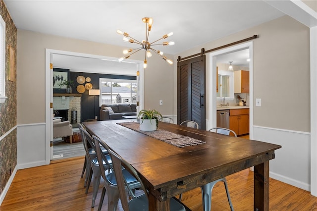 dining room with a barn door, light wood finished floors, a brick fireplace, and a notable chandelier