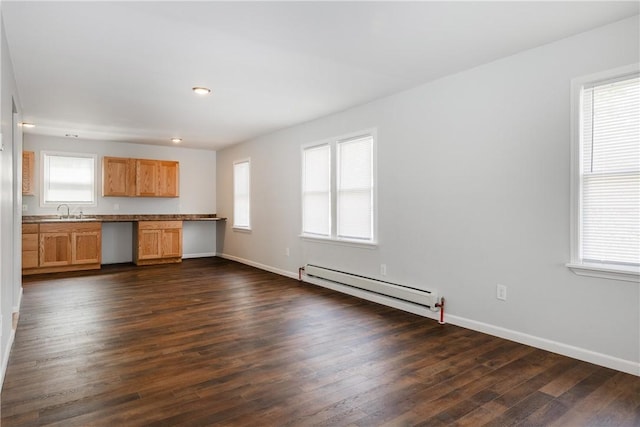 unfurnished living room featuring baseboards, a baseboard heating unit, dark wood-style floors, and a wealth of natural light
