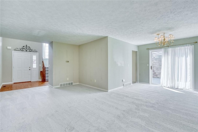 unfurnished living room with a textured ceiling, carpet flooring, a chandelier, and visible vents
