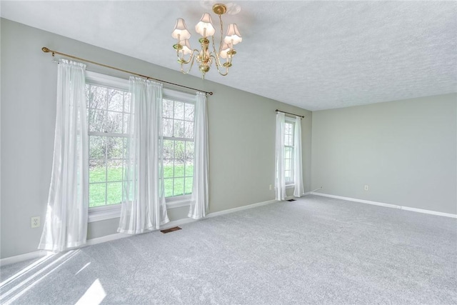 spare room with visible vents, plenty of natural light, an inviting chandelier, and carpet