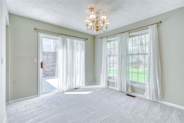carpeted spare room with a textured ceiling, a chandelier, and plenty of natural light