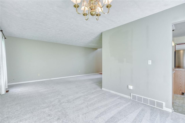 empty room featuring a textured ceiling, a notable chandelier, visible vents, and baseboards