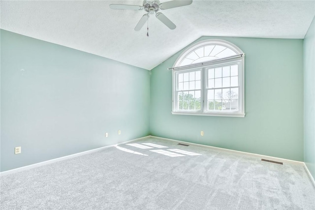 carpeted spare room featuring a ceiling fan, a textured ceiling, visible vents, vaulted ceiling, and baseboards