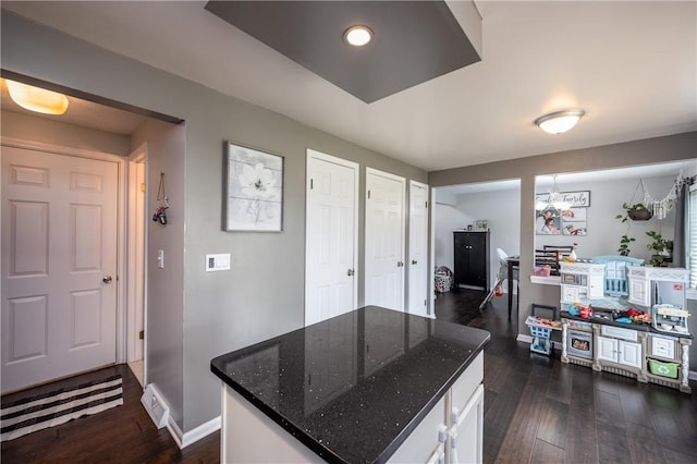 kitchen featuring a kitchen island, visible vents, white cabinets, dark wood-style floors, and dark stone countertops