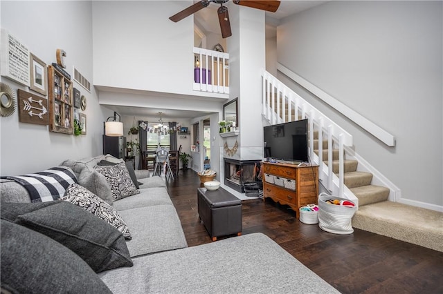 living room featuring stairs, a high ceiling, wood finished floors, and ceiling fan with notable chandelier