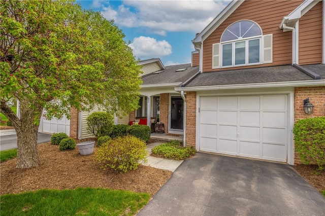 view of front of house featuring a shingled roof, an attached garage, brick siding, covered porch, and driveway