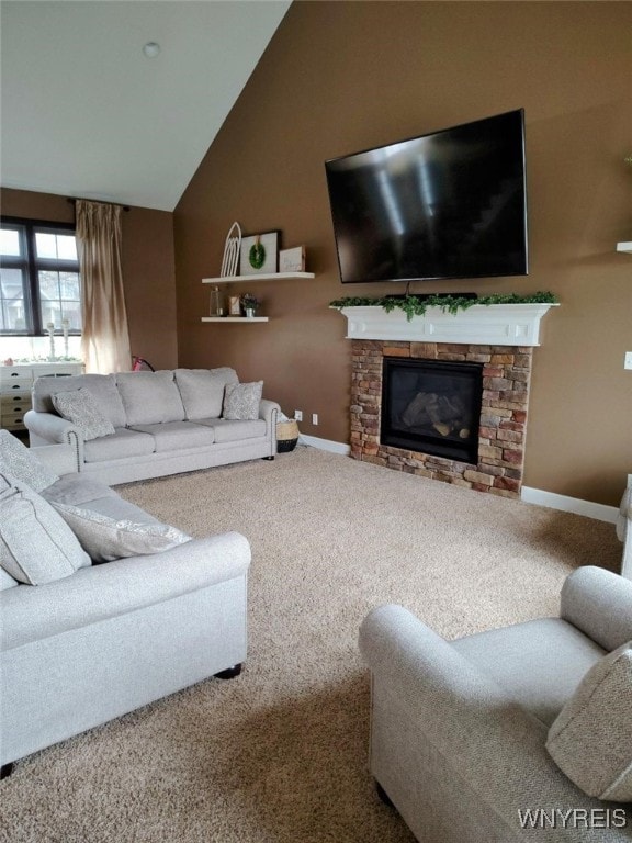 living room with baseboards, carpet floors, vaulted ceiling, and a stone fireplace