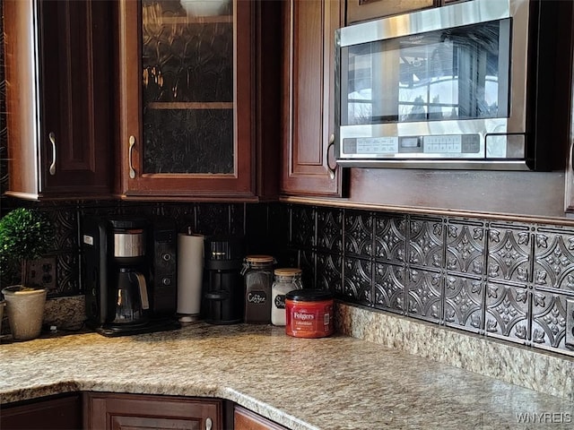 kitchen featuring light countertops, stainless steel microwave, backsplash, and glass insert cabinets