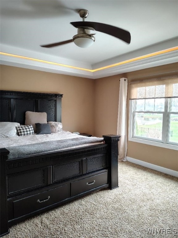 bedroom featuring light colored carpet, a raised ceiling, baseboards, and ceiling fan