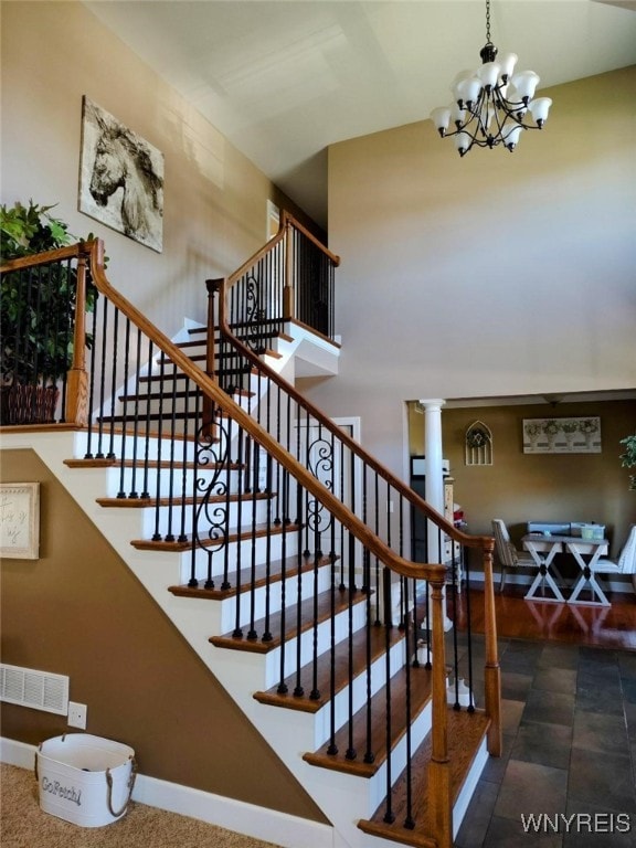 staircase featuring visible vents, a towering ceiling, baseboards, ornate columns, and a notable chandelier