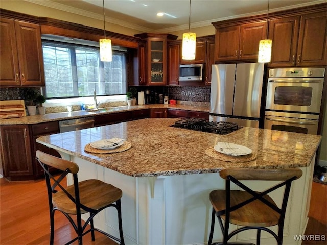 kitchen with light stone countertops, hanging light fixtures, a breakfast bar, a sink, and stainless steel appliances